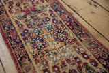 Detail of an antique Kerman rug: intricate cochineal red, navy, apricot blossom patterns with wear.