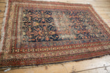Vintage Malayer rug corner reveals tattered fringe, wear to foundation, navy, red, ivory Herati design.