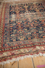 Worn corner of vintage Malayer rug with exposed navy Herati field, geometric red border, and tattered fringe.