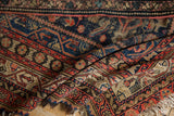 Folded vintage Malayer rug displaying Herati pattern, navy, red, ivory, and tattered fringe.