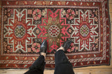 Vintage Caucasian geometric rug with starburst medallion in red, pink, charcoal, framing feet.