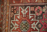 Geometric reciprocating wave and leaf borders of a vintage Caucasian rug in burgundy, pink, and charcoal.