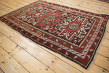 Vintage Caucasian rug corner showing geometric wave and finned leaf borders in burgundy red.