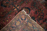Vintage Lilihan rug corner folded, showing plum floral pile, woven foundation, and tattered edges.