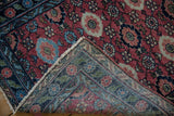 Hand-knotted vintage Lilihan rug folded, showing cherry red field, blue border, and weave.