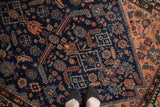 Deep indigo Malayer rug field, featuring geometric blossoms, animal figures, and blush accents.