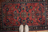 Vintage Lilihan rug showcasing a quatrefoil medallion, red field, and blue palmettes with shoes for scale.