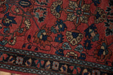 Intricate floral motifs and serrated palmettes on brick red field with dark navy border.