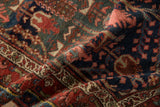 Textured fold of vintage Hamadan rug displays rich navy, madder red, and blush floral patterns.