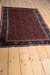 Angled perspective of a vintage Persian Engelas rug showing its rust and navy blue Herati design.