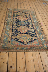 Corner detail of a vintage Malayer rug with navy, sand, blush motifs and frayed side selvage.