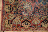 Corner detail of vintage Sarouk rug, dusty rose floral field, navy border, tattered fringe.
