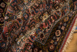 Folded vintage Hamadan rug pile with dusty red, navy blue, and gold Herati pattern details.