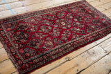 Tattered edge of vintage American Sarouk runner showing cherry red and turquoise floral motif.
