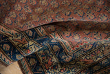 Folded vintage Hamadan rug showing navy blue border and dusty raspberry red boteh field.