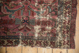 Worn corner of vintage Mehreban rug, revealing ivory foundation and tattered edges with plum and teal tones.