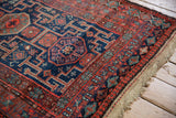 Vintage Kurd rug detail showing navy geometric stepped medallions, brick red field, and worn fringe.
