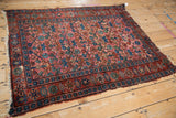 Worn lower corner of a vintage Persian Lilihan rug, showing sapphire blue motifs and tattered edges.