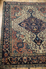 Antique Farahan Sarouk rug's detailed border with navy arabesques, blush palmettes, and textured pile.