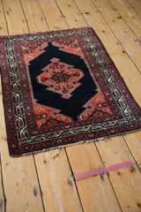 Angled view of a vintage Persian Malayer rug with its dark navy medallion and brick red border.