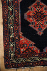 Geometric vine border and serrated red corner spandrel on a vintage navy blue Persian Malayer rug.