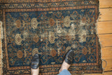 Textured Malayer rug detail, showcasing worn deep blue field, repeating design, and tattered edges.