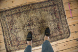 Worn corner of antique Kerman rug, revealing hand-knotted foundation and faded ivory, navy, cochineal motifs.