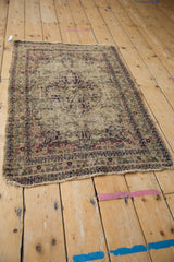 Tattered edge and exposed foundation of an antique Kerman rug with faded ivory, navy, and red motifs.