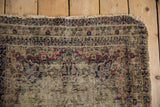 Antique Kerman rug with exposed ivory foundation, tattered edge, faded navy and cochineal patterns.