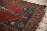 Malayer rug corner close-up, with foundation wear on red field and tattered fringe.