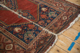 Vintage Malayer rug detail: cherry red field with foundation showing, indigo geometric motifs, tattered fringe.
