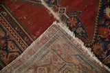Vintage Malayer rug corner: worn cherry red pile, indigo border, tattered fringe, woven foundation.