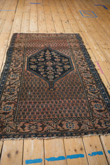 Antique Malayer rug corner: dusty blush boteh field, navy vinery border, and worn fringe.