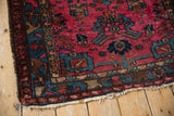 Corner of vintage Mehreban rug, featuring raspberry field, sapphire blue geometric border, and fringe.