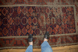 Antique Belouch rug runner's tribal madder red and navy patterns with worn pile, exposed foundation.