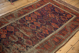 Worn antique Belouch rug's madder red and navy geometric patterns with exposed foundation.