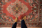 Vintage Persian Arak rug's central floral medallion with blush patterns on a pale cherry red field.