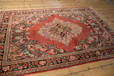 Vintage Arak rug corner detail, pale cherry red field, blush floral spandrel, dark navy border.