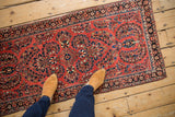 Dense floral bouquets in navy blue and ivory cover the brick-red field of this vintage Sarouk runner.