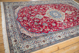 Angled corner view of a vintage Nain carpet, showing the navy spandrel and scrolling vinery border.