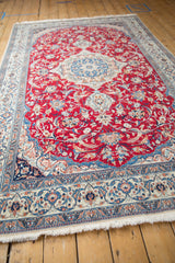 Angled view of a vintage Nain carpet highlighting its cherry red field and elaborate blue medallion.