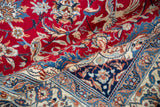 Vibrant cherry red field with scrolling vinery folded over the intricate ivory and navy blue border of a Nain carpet.