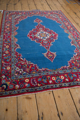 Angled view of a fine Kashan rug showcasing the scalloped red floral medallion on an open blue field.