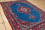 Angled perspective of a vintage Kashan rug, highlighting the cherry red border and blue scalloped medallion.