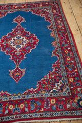 Angled perspective of a Kashan rug's scalloped medallion and red floral blossom border.
