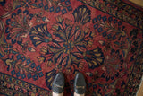 Vintage Lilihan rug's cherry red field, navy and gold arabesque pattern, even wear, with loafers.