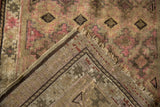 Folded corner of vintage Caucasian rug, showing geometric guls, pink motifs, woven back, and worn fringe.