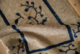 Folded antique Chinese Peking rug reveals plush beige pile and cobalt blue floral pattern.