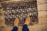 Antique Anatolian rug fragment with water motifs and worn edges, shown on a floor for scale.