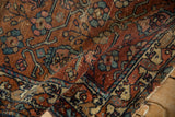 Folded vintage Persian Mehreban rug revealing textured madder red, blue, and blush vine blossom pattern.